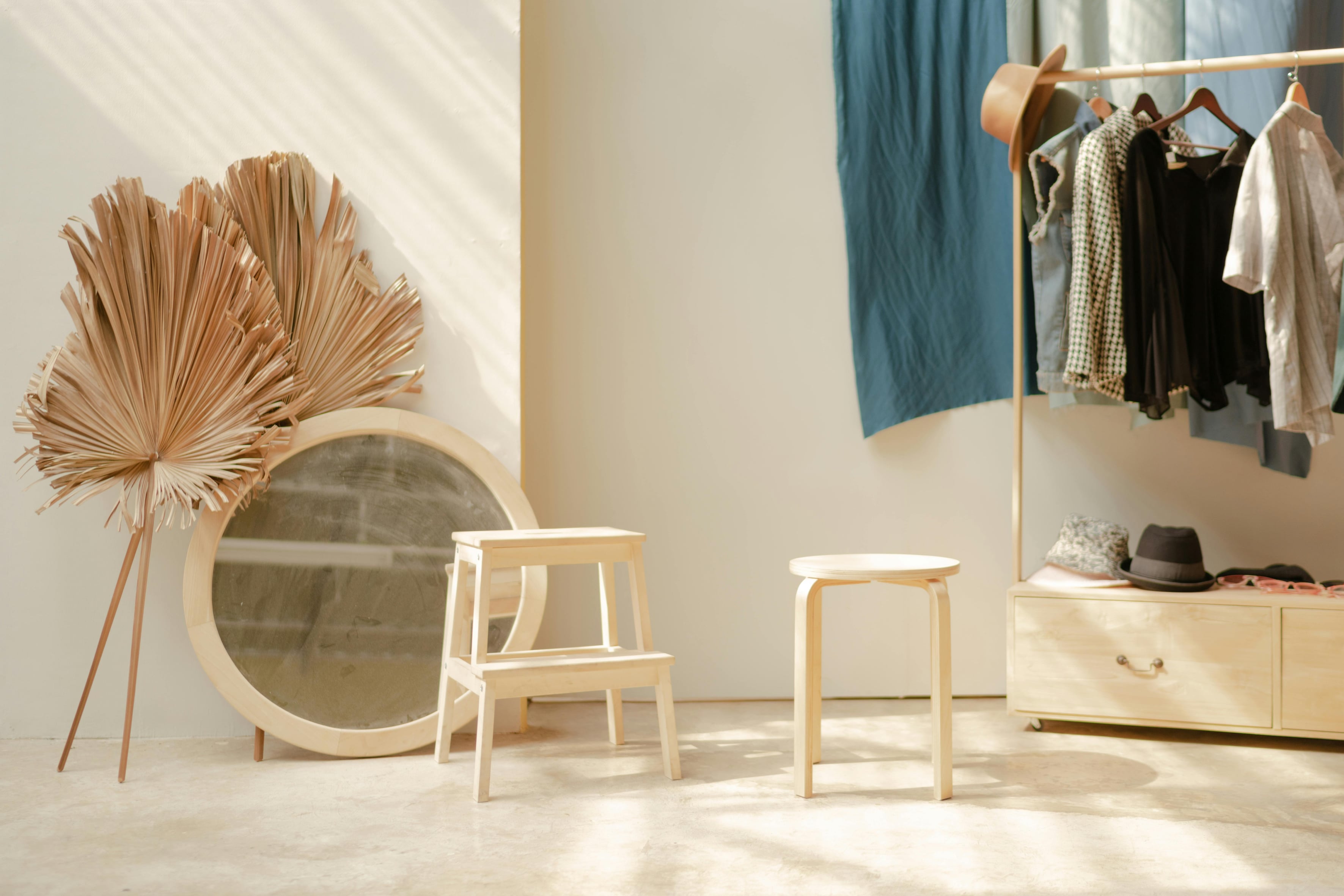 Sunlit room with a mirror, two stools, and a coat rack with clothes