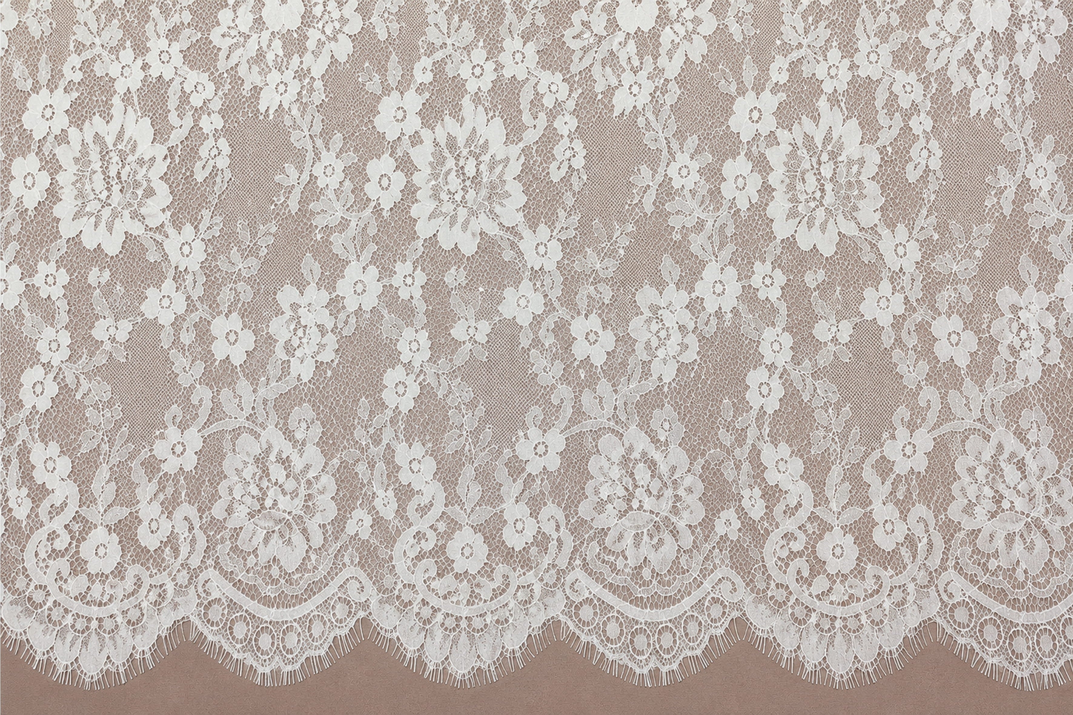 White Chantilly lace with an intricate floral pattern displayed against a soft pink background