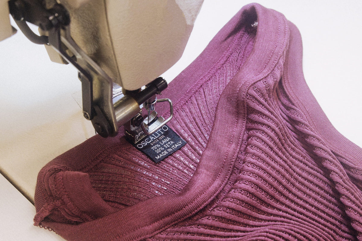 Oscalito label showing material and origin information, sewn onto a cherry-coloured wool and silk openwork garment